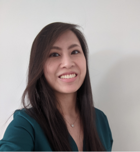 A women smiles to the camera with long brown hair. She is wearing a teal blazer.